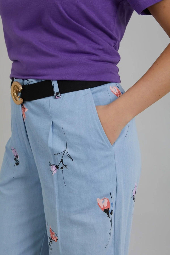 Pantalon large en denim avec imprimé floral, porté avec un t-shirt violet et ceinture noire.