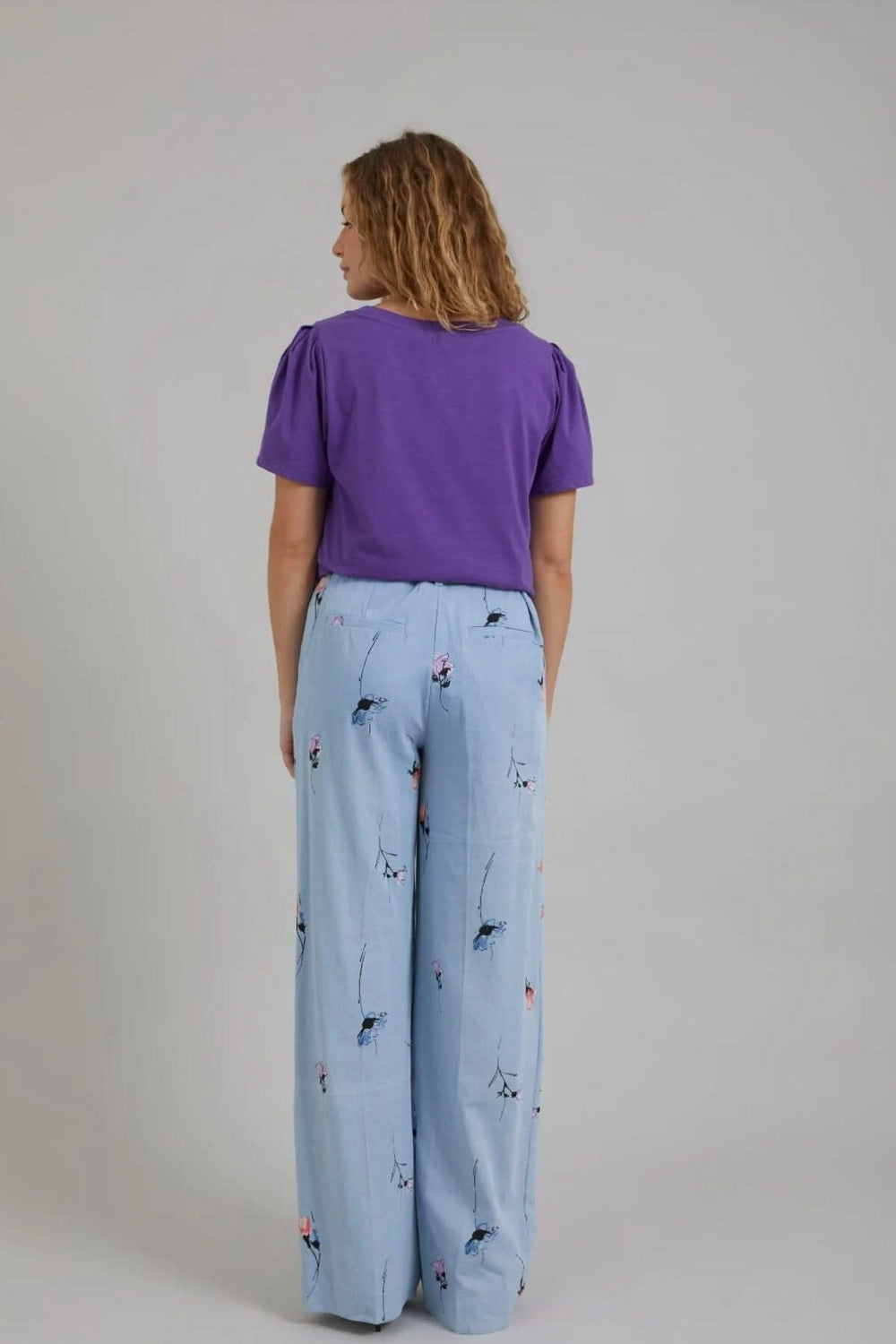 Femme vue de dos portant un t-shirt violet et un pantalon large en denim imprimé floral.