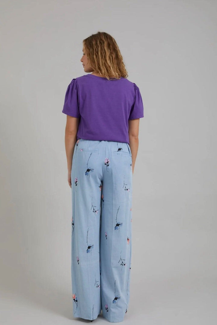 Femme vue de dos portant un t-shirt violet et un pantalon large en denim imprimé floral.