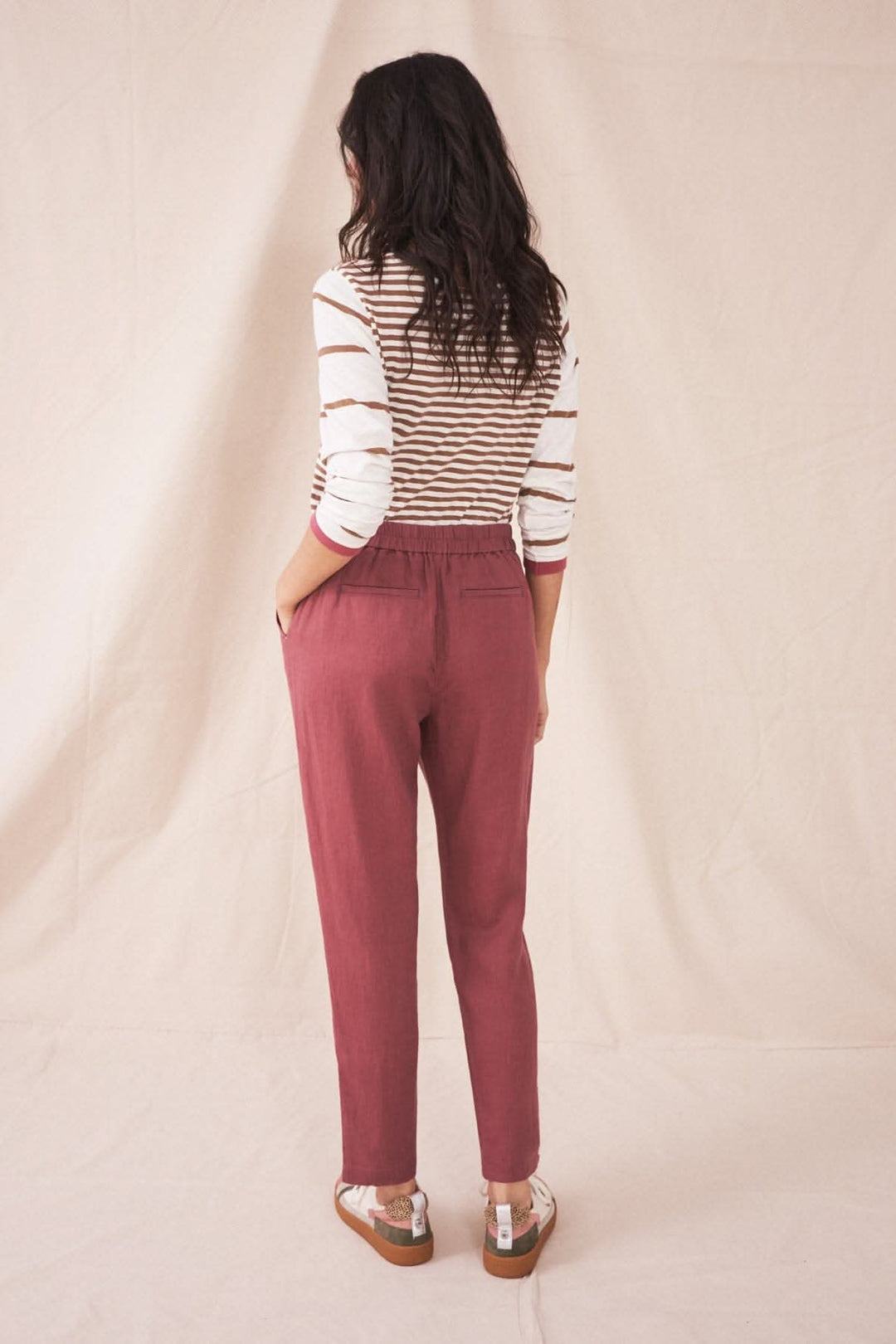 Femme portant le pantalon Maddie en lin rose, vu de dos, avec un top rayé sur fond neutre.