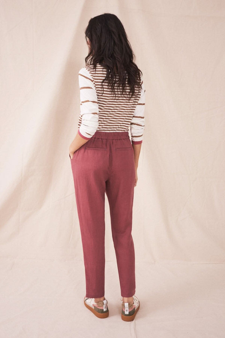 Femme portant le pantalon Maddie en lin rose, vu de dos, avec un top rayé sur fond neutre.