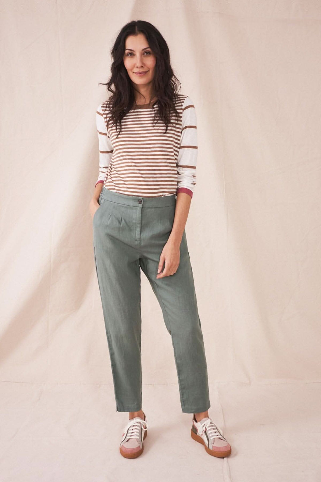 Femme portant le pantalon Maddie en lin vert avec une shirt à rayures et des baskets, idéale pour temps chaud.