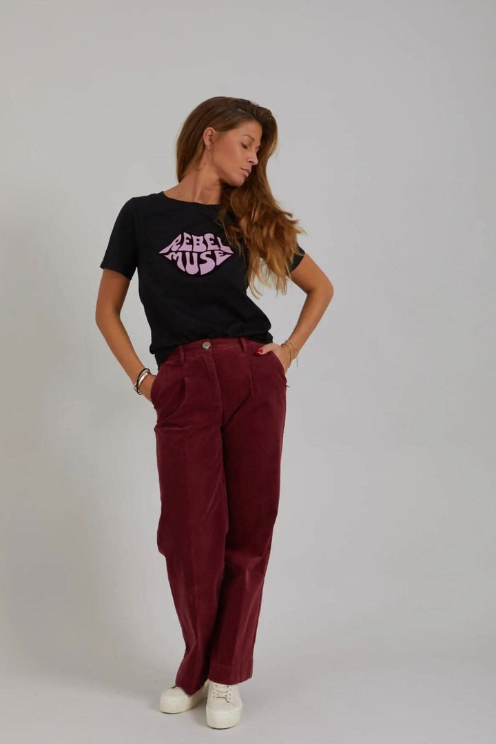 Femme portant le pantalon Petra en velours côtelé bordeaux avec un t-shirt noir sur fond neutre.