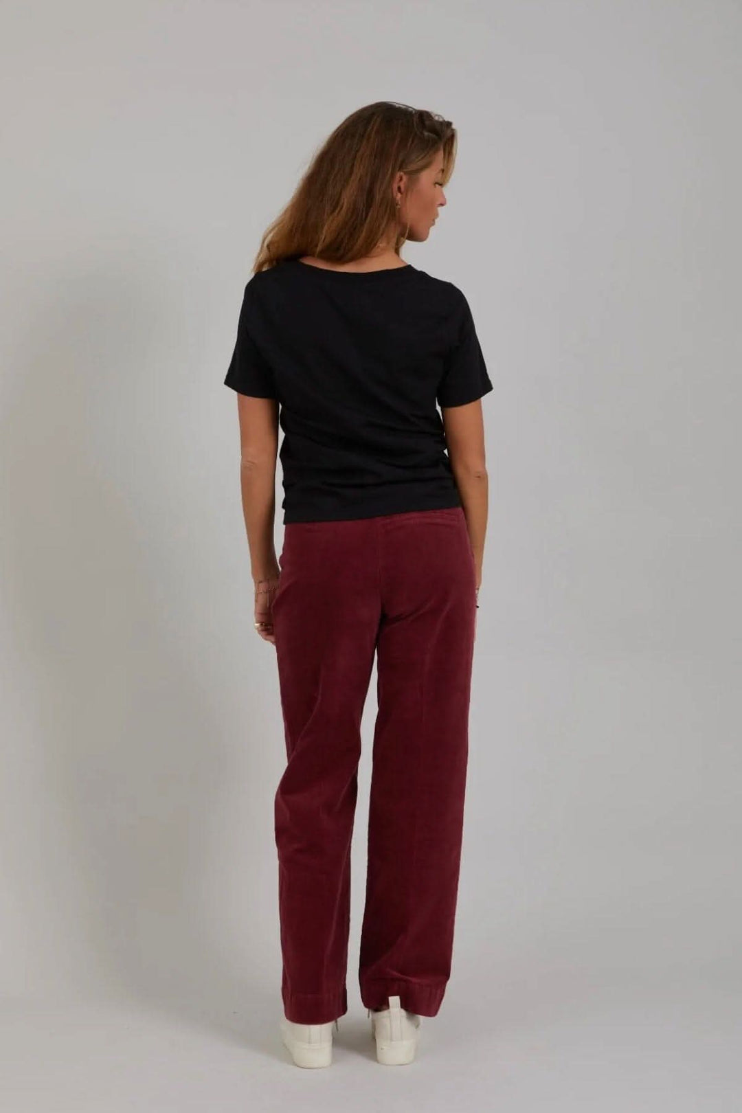 Femme vue de dos portant le pantalon Petra en velours côtelé bordeaux avec un t-shirt noir.