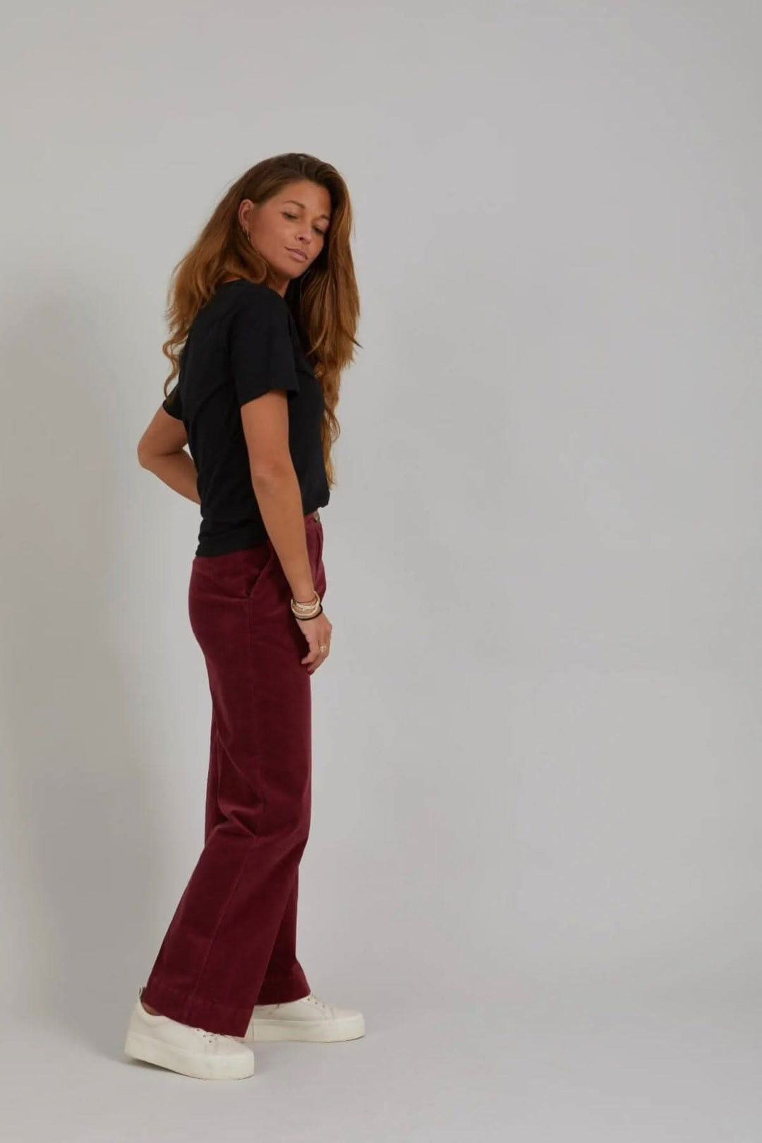 Femme portant le pantalon Petra de velours côtelé, jambes larges, ajusté à la taille, en couleur bordeaux.