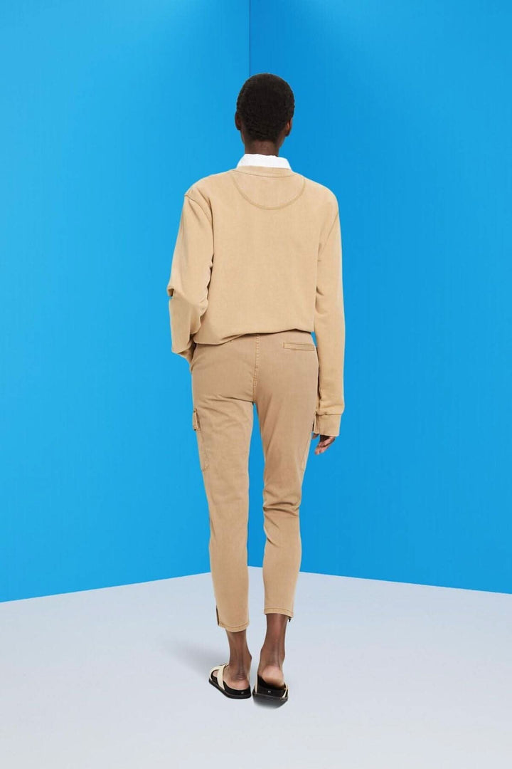 Femme portant un pantalon taille mi-haute style cargo beige, vue de dos, avec un fond bleu.