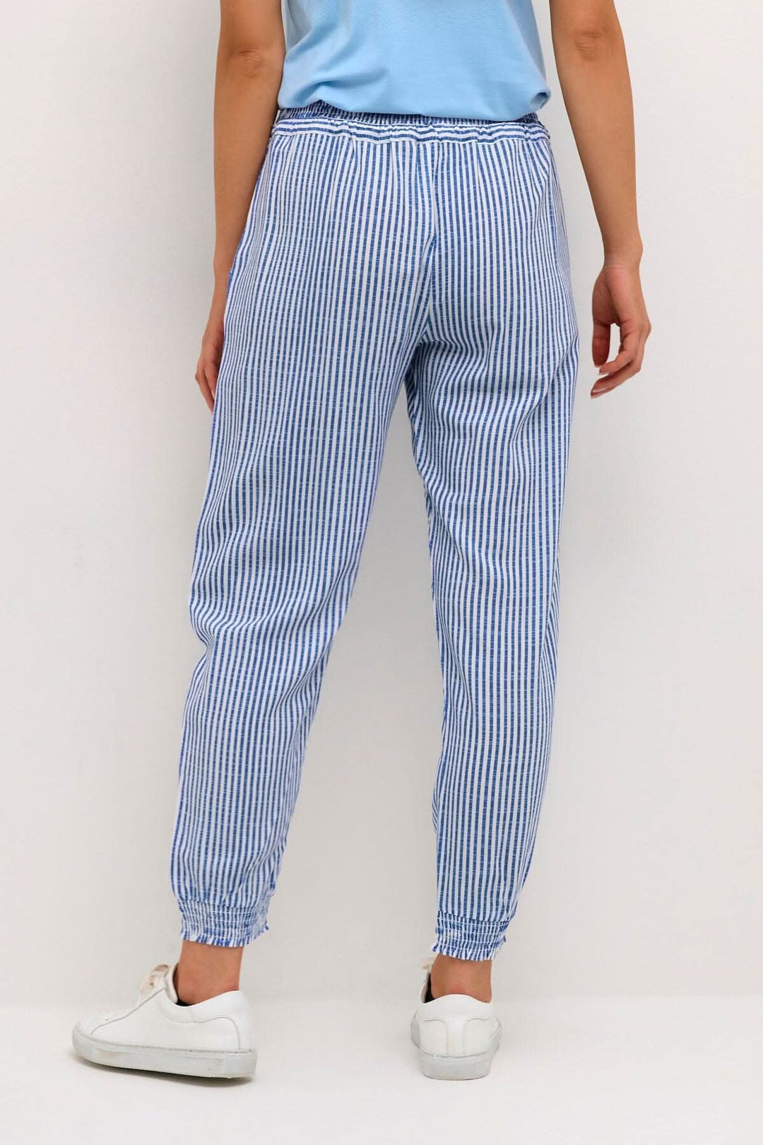 Pantalon Willis à rayures bleues, avec taille élastique et chevilles resserrées, porté avec des baskets blanches.