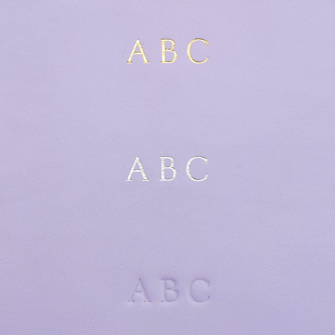 Détails d'une couverture en cuir violet avec le texte 'ABC' en doré, argenté et en relief.