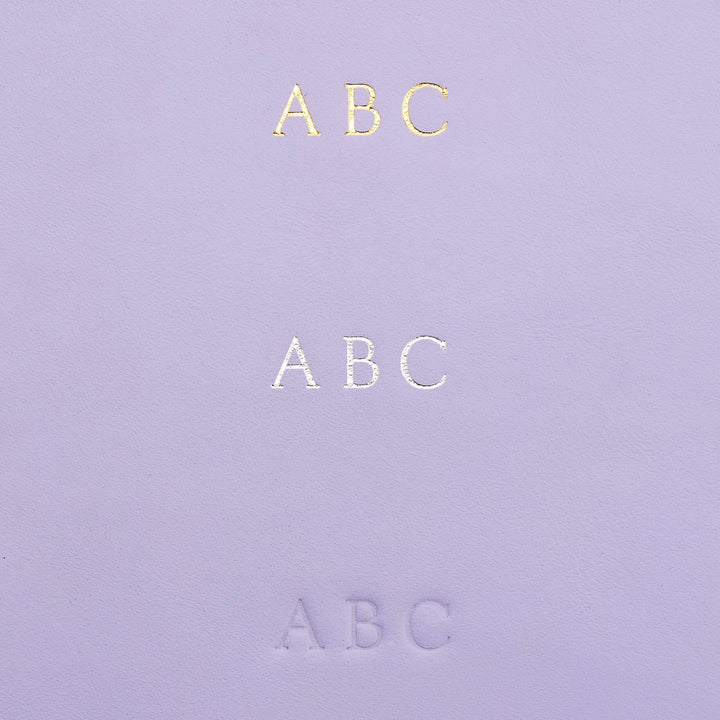 Détails d'une couverture en cuir violet avec le texte 'ABC' en doré, argenté et en relief.