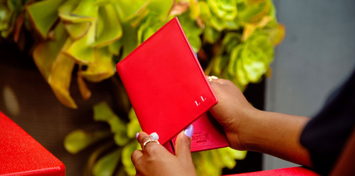 Femme tenant un étui à passeport rouge en cuir près de plantes vertes.