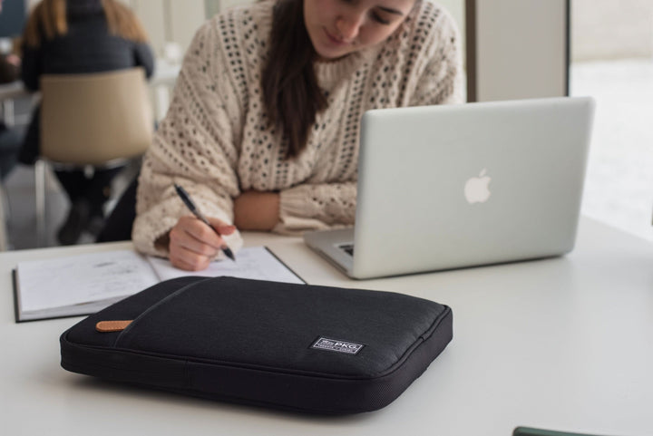 Pochette pour ordinateur portable PKG Stuff sur une table, avec une étudiante en train de travailler.