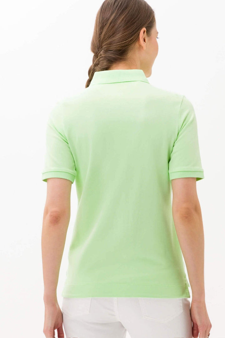 Femme portant un polo Cleo vert clair, vue arrière, mettant en avant la coupe confortable et le style estival.
