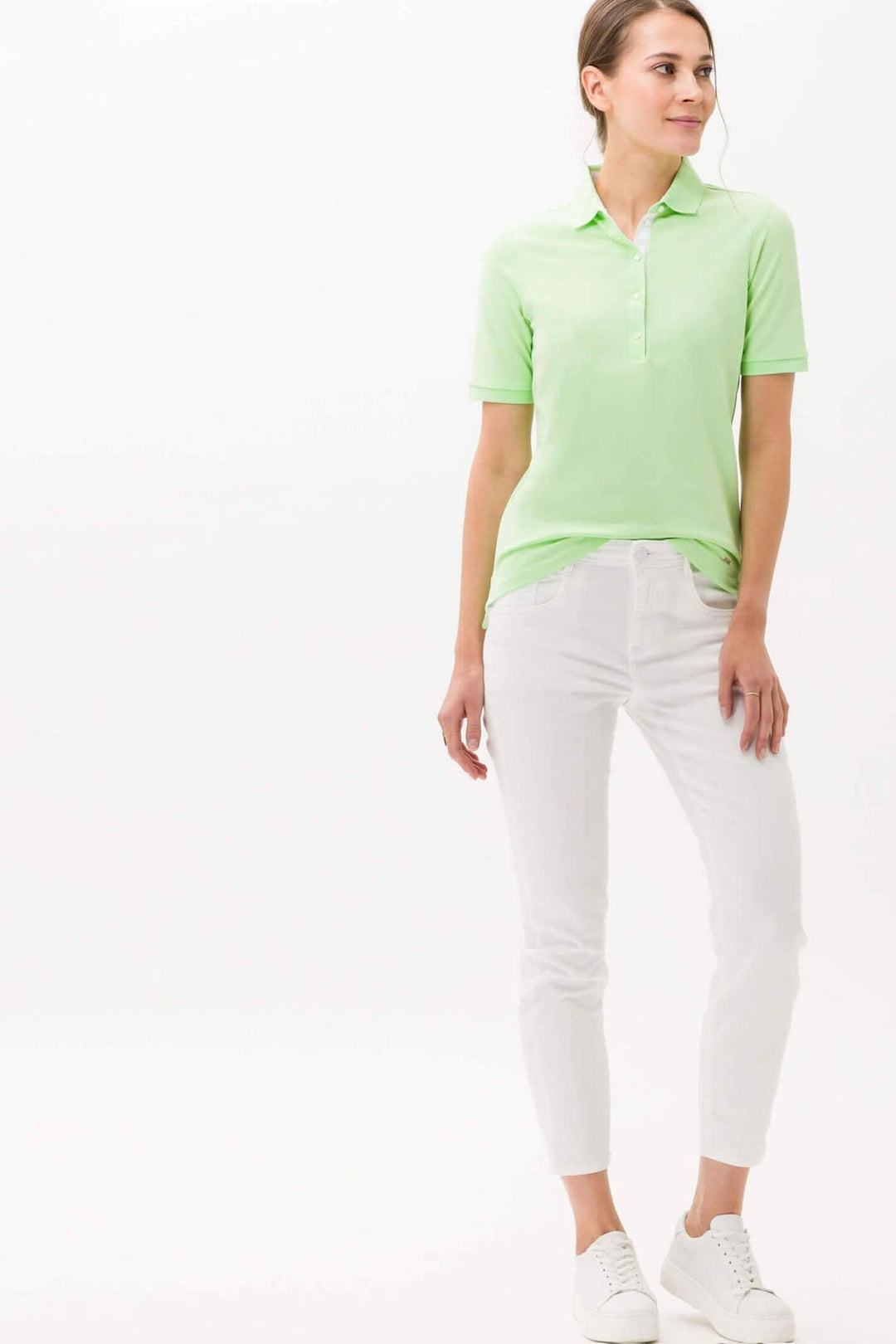 Femme portant un polo Cleo vert clair, associé à un pantalon blanc, idéal pour un look estival élégant.
