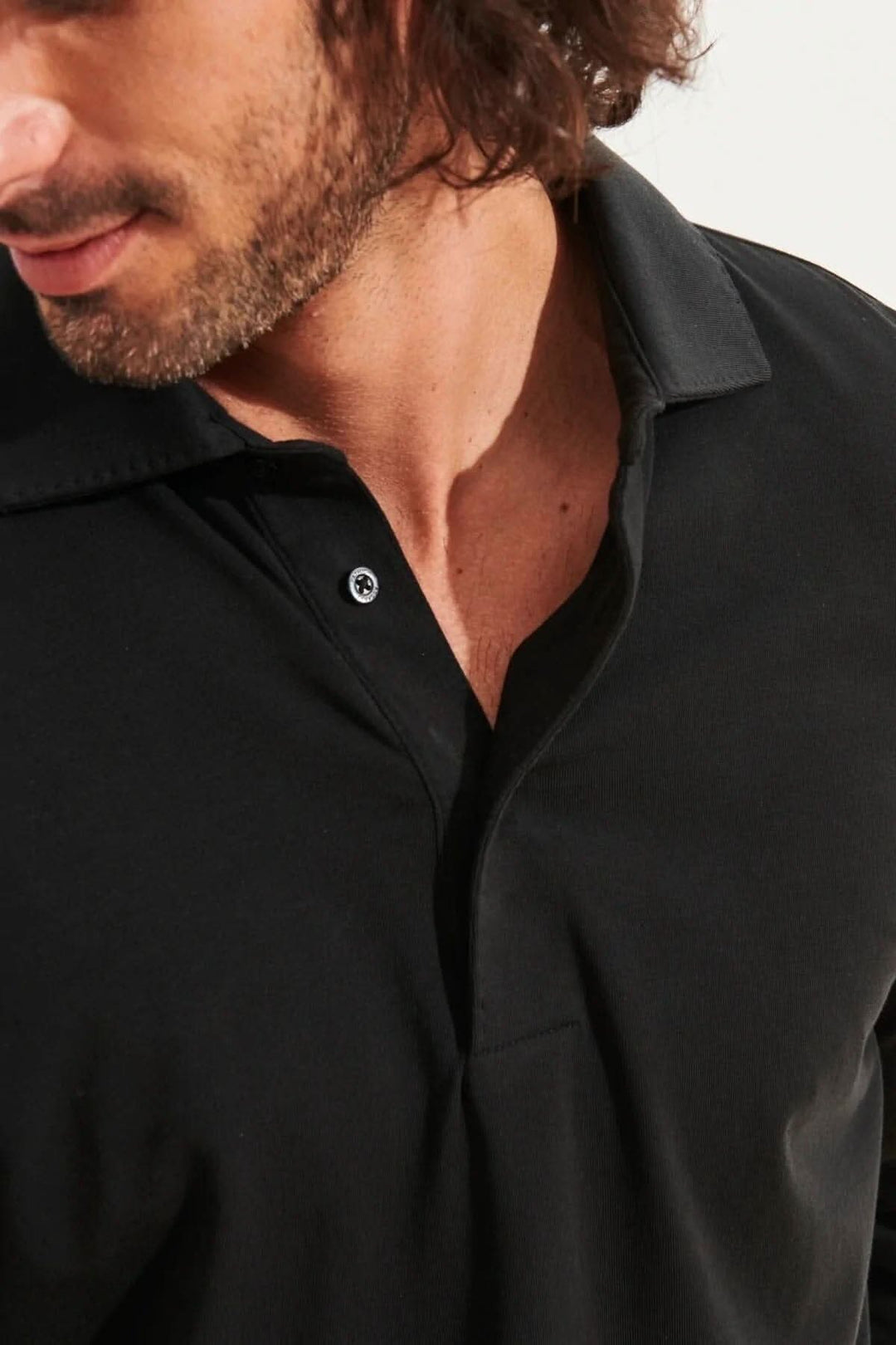 Homme portant un polo noir à manches longues, en jersey de coton pima, col surpiqué.