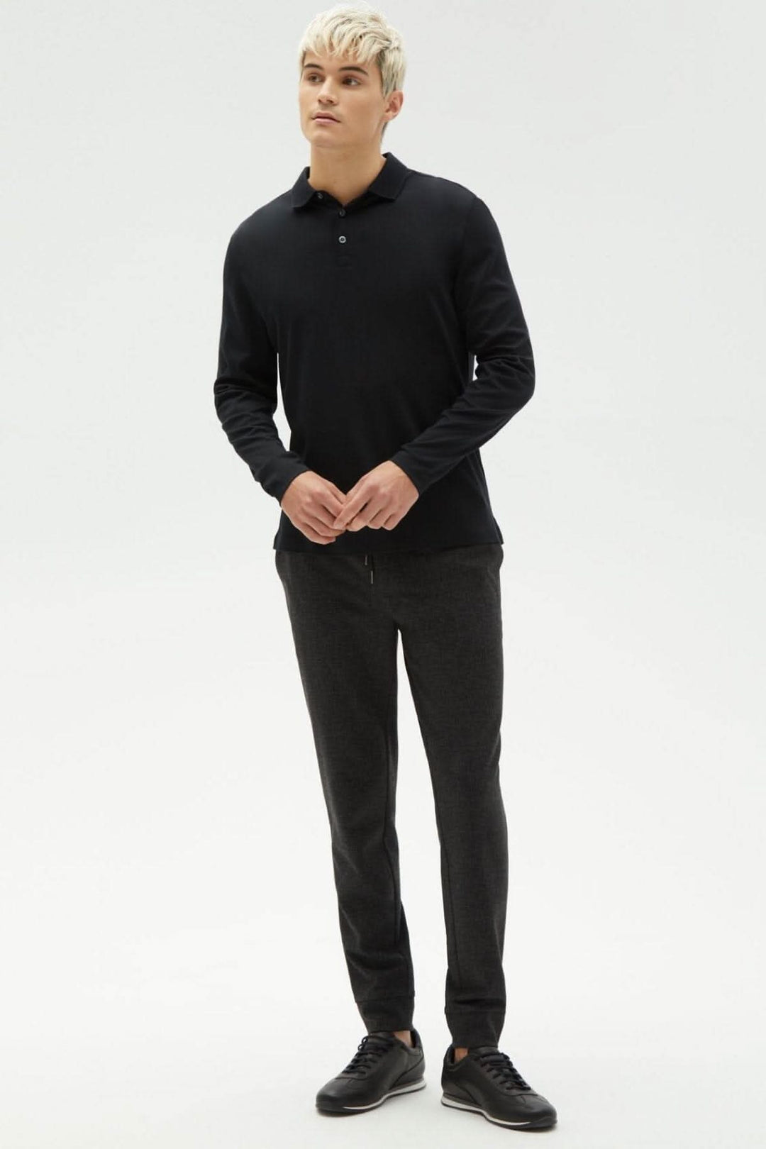 Homme portant un polo Georgia noir et un pantalon gris, style décontracté et moderne.