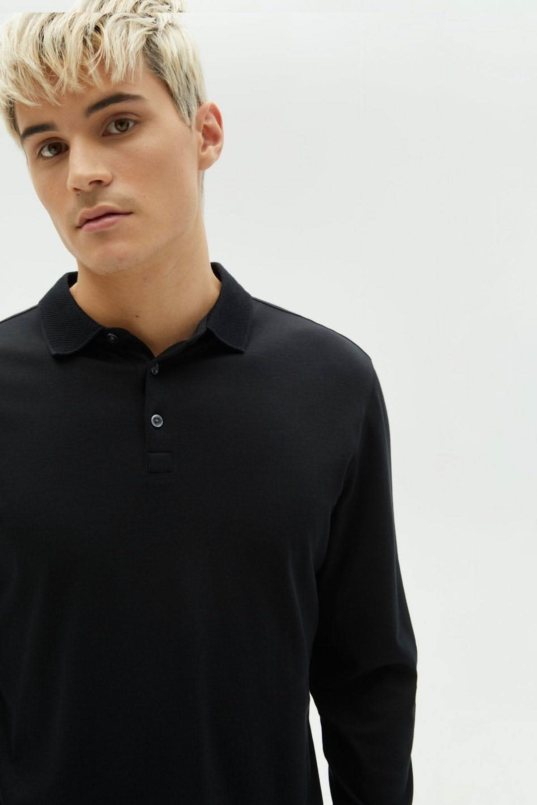 Homme portant un polo noir à manches longues, col classique, fabriqué en coton Pima pour un confort ultime.