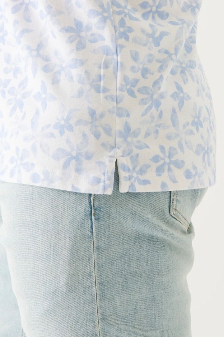 Polo imprimé en coton pima extensible avec motif floral bleu, porté avec un jean clair.