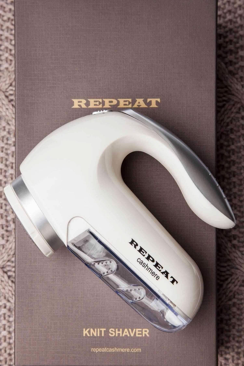 Rasoir à laine électrique REPEAT pour enlever bouloches et fibres des vêtements en laine, avec récipient transparent.