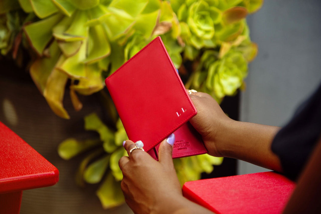 Hands holding a red RFID blocking vaccine card passport wallet against a vibrant green backdrop.