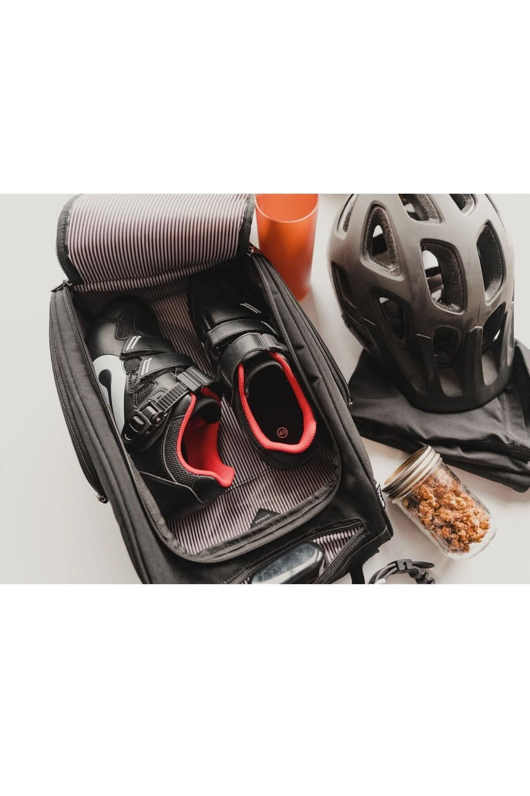 Sac à chaussures ouvert avec des chaussures noires, un casque et un gobelet, idéal pour les cyclistes.