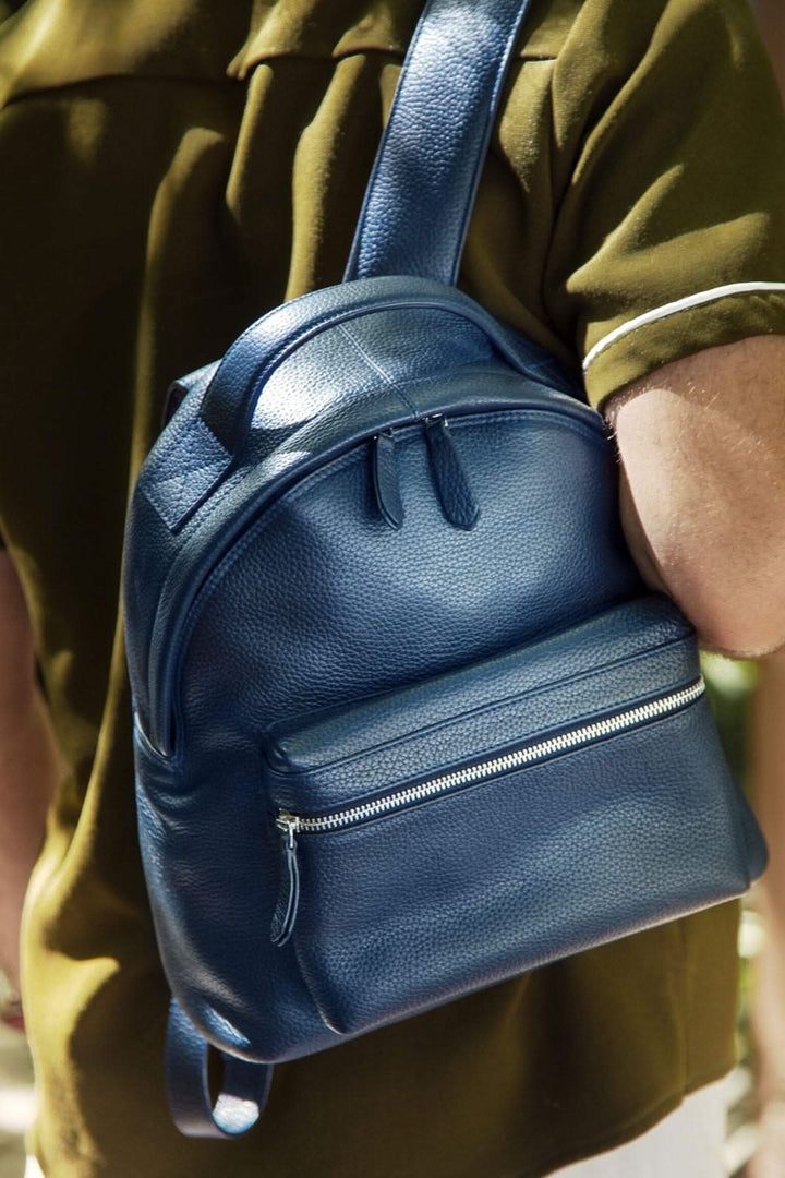 Sac à dos de voyage compact en cuir bleu avec compartiments pratiques, porté sur l'épaule.