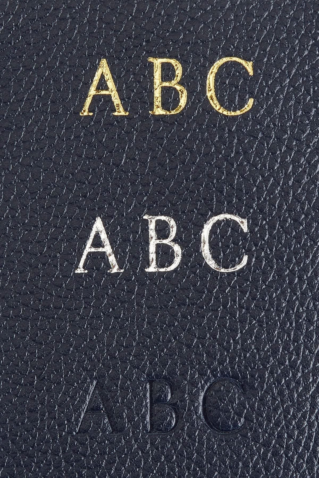 Détails de gravure sur cuir avec lettres ABC en doré, argenté et embossé sur fond bleu.