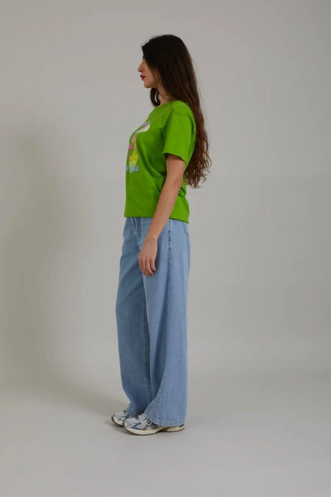 Femme portant un t-shirt vert avec imprimé champignon, jeans larges, vue latérale.