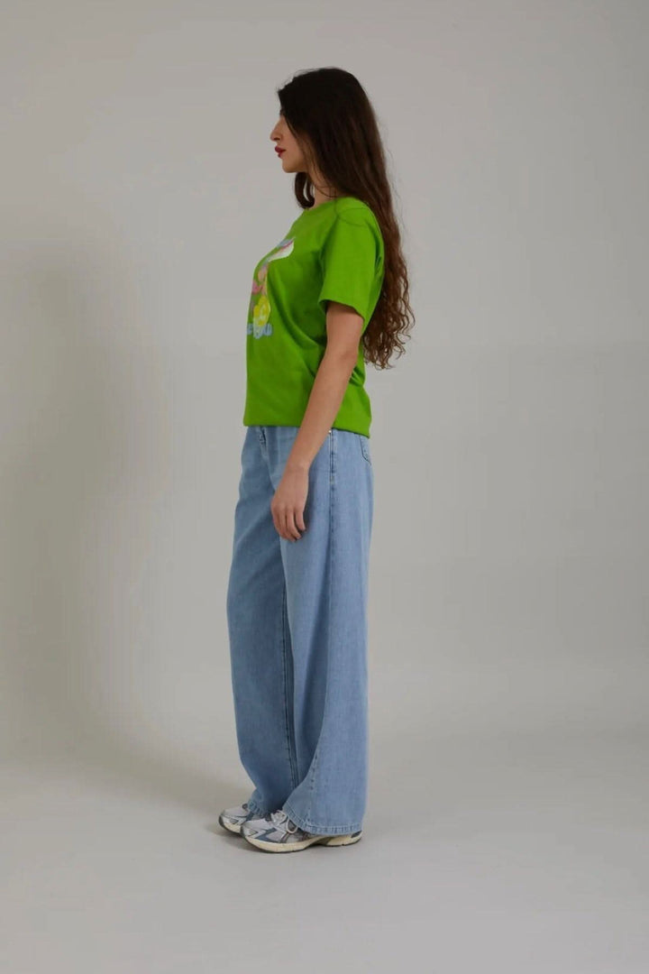 Femme portant un t-shirt vert avec imprimé champignon, jeans larges, vue latérale.