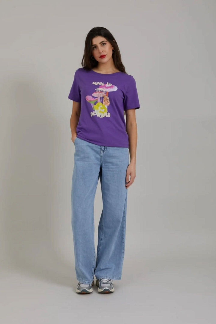 T-shirt violet avec imprimé champignon, porté avec pantalon large et baskets, en style décontracté.