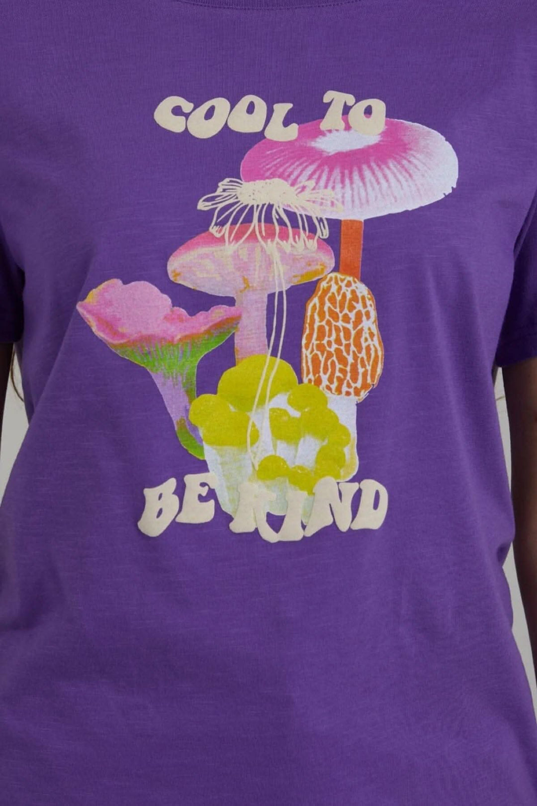T-shirt violet avec imprimé champignon coloré et texte 'Cool to be kind' en lettres stylisées.