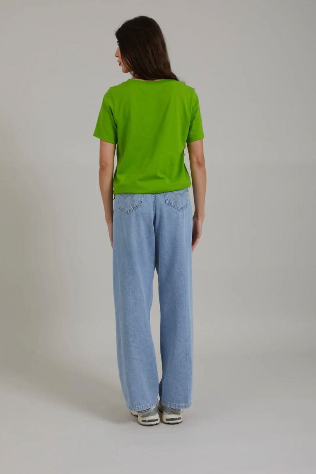Femme vue de dos portant un t-shirt vert avec jeans larges, style décontracté.