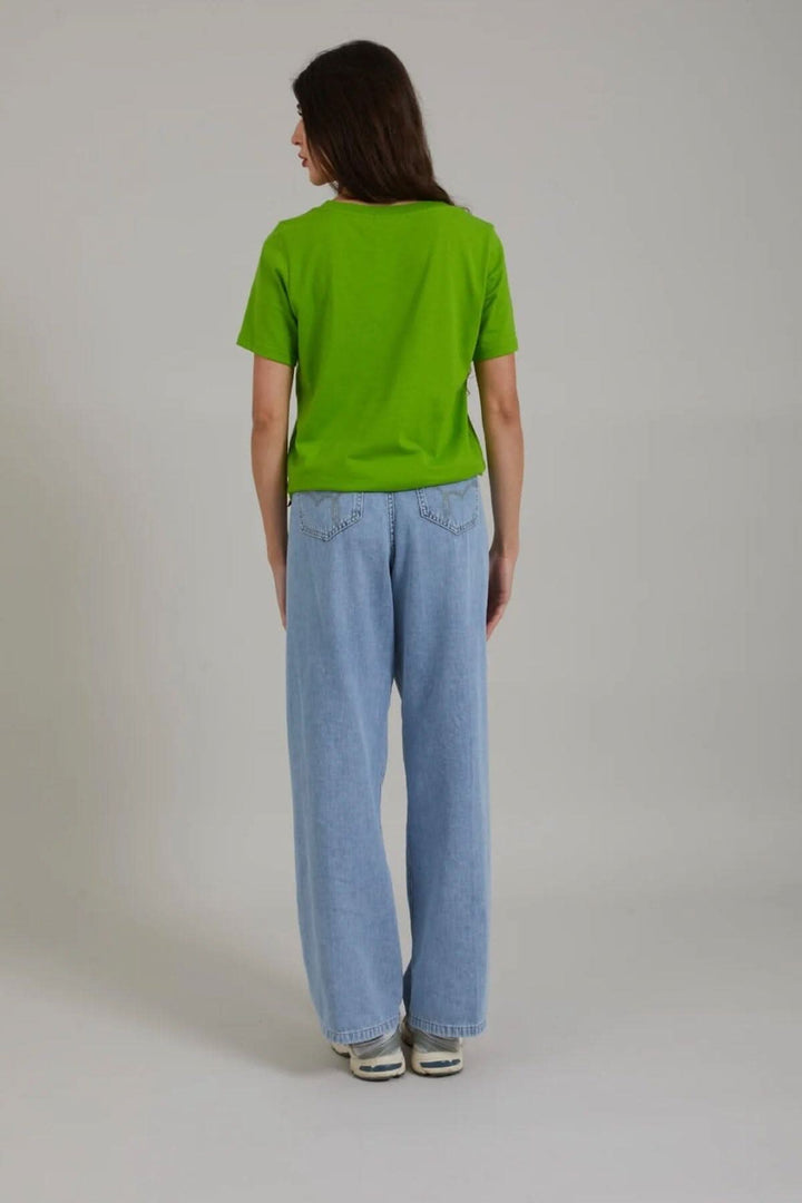 Femme vue de dos portant un t-shirt vert avec jeans larges, style décontracté.