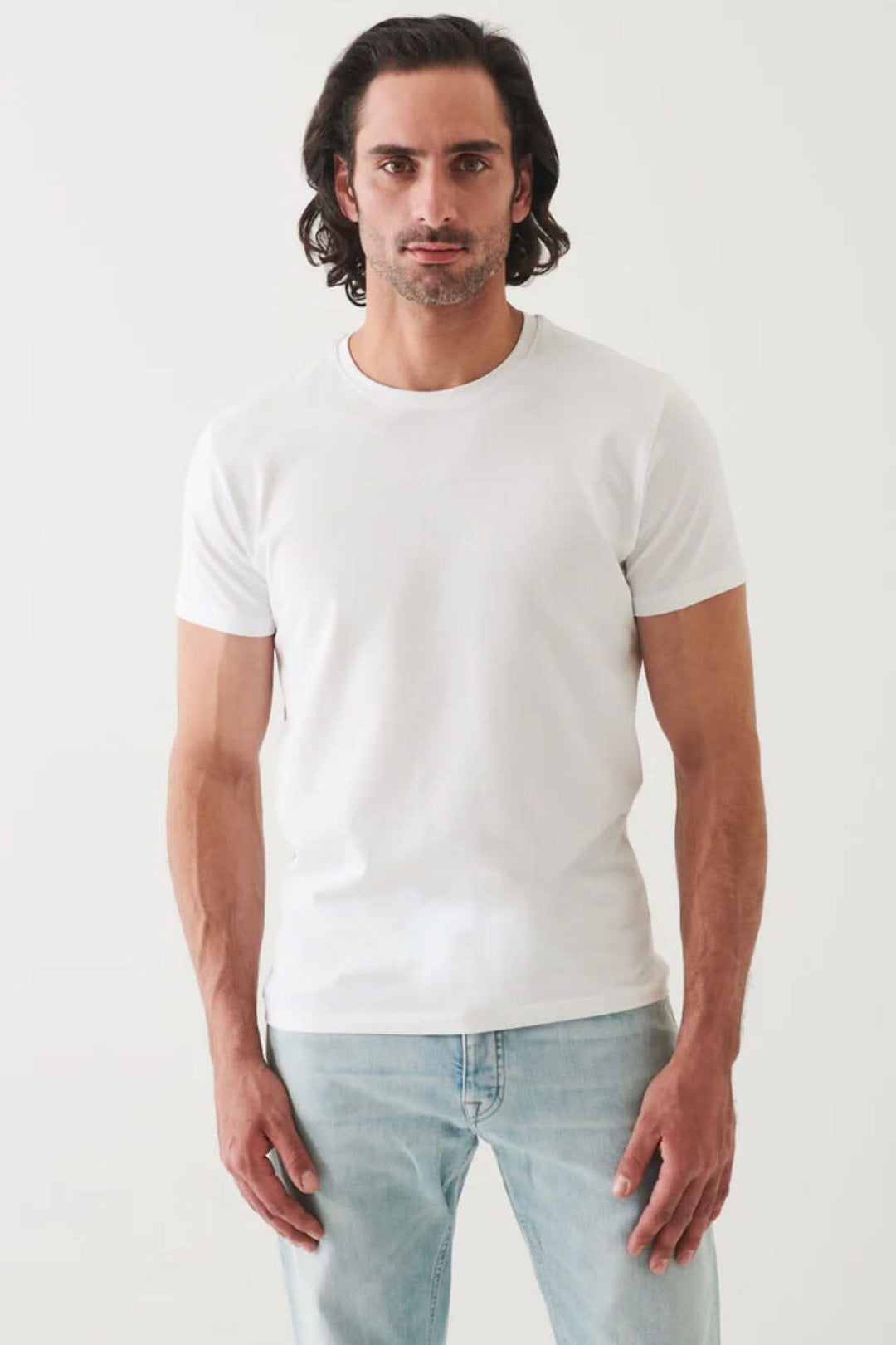 Homme portant un T-shirt basique blanc à la coupe moderne et style minimaliste, avec jeans.