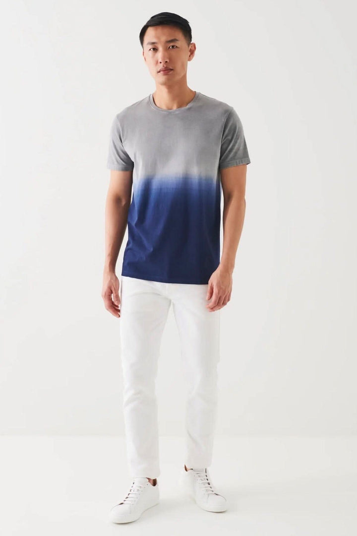 Homme portant un t-shirt en coton pima stretch dégradé avec un jean blanc et des sneakers.