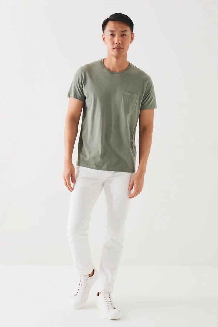 Homme portant un t-shirt léger en coton pima vert avec poche, associé à un pantalon blanc.