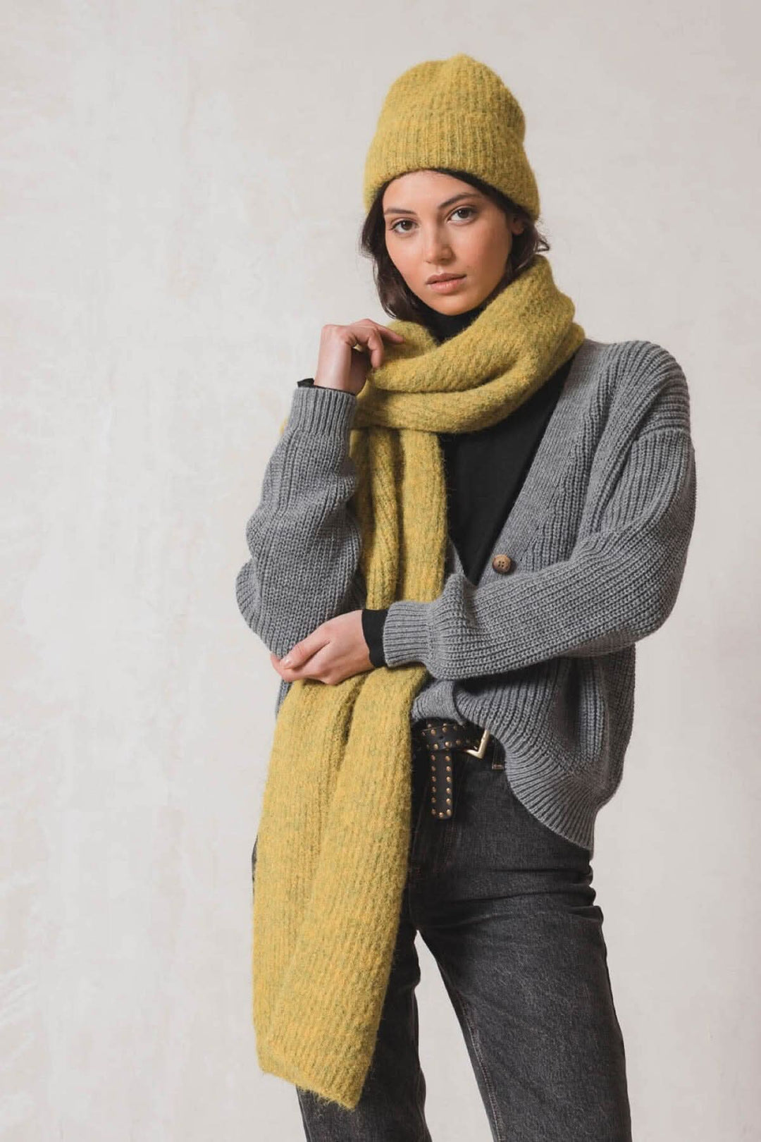 Femme portant une tuque en tricot jaune, écharpe et cardigan gris, prête pour un look chic et réchauffant.