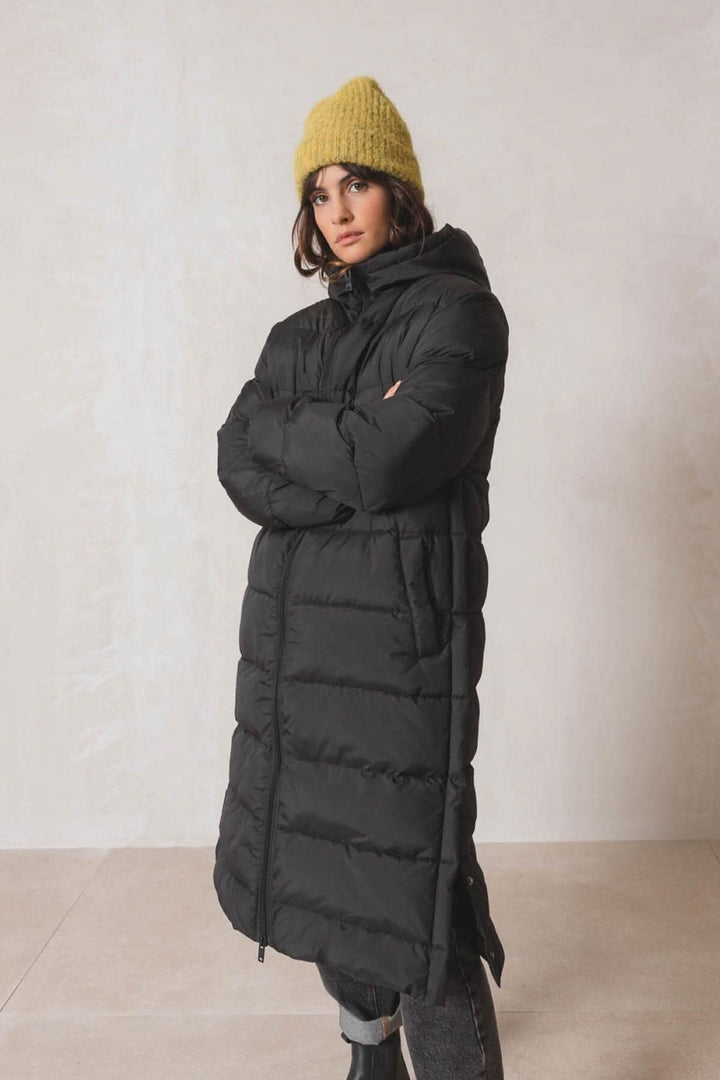 Femme portant un manteau noir matelassé avec une tuque en tricot jaune, style décontracté pour l'hiver.