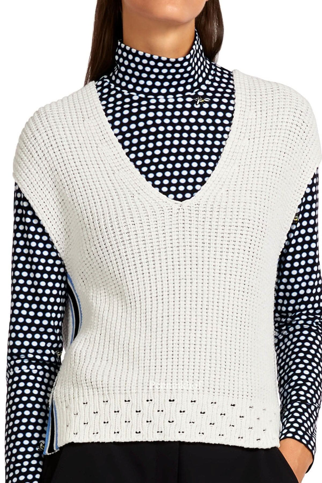 Veste en tricot blanc à col en V, portée sur un t-shirt à pois, avec ourlet large et biais rayé.