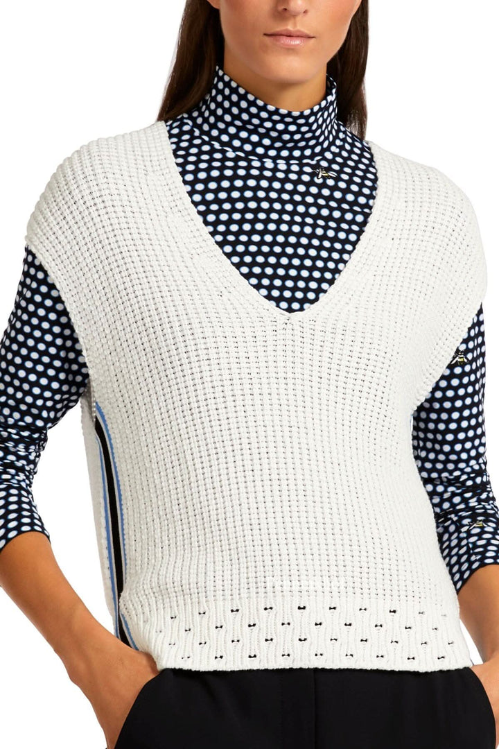 Veste en tricot blanche avec col en V, fentes sur les côtés, portée sur un sous-pull à pois.