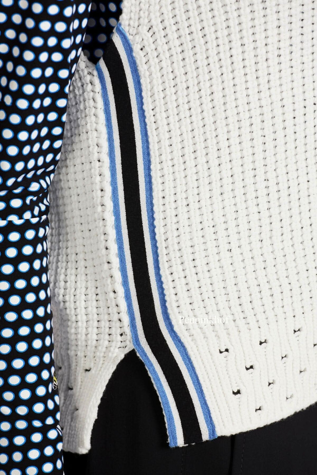 Détail d'une veste en tricot blanche avec ourlet ouvert et biais rayé bleu et noir.