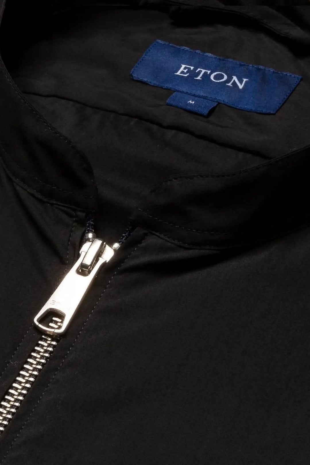 Gros plan sur une veste noire ETON avec zip et étiquette, idéale pour la superposition et le style contemporain.
