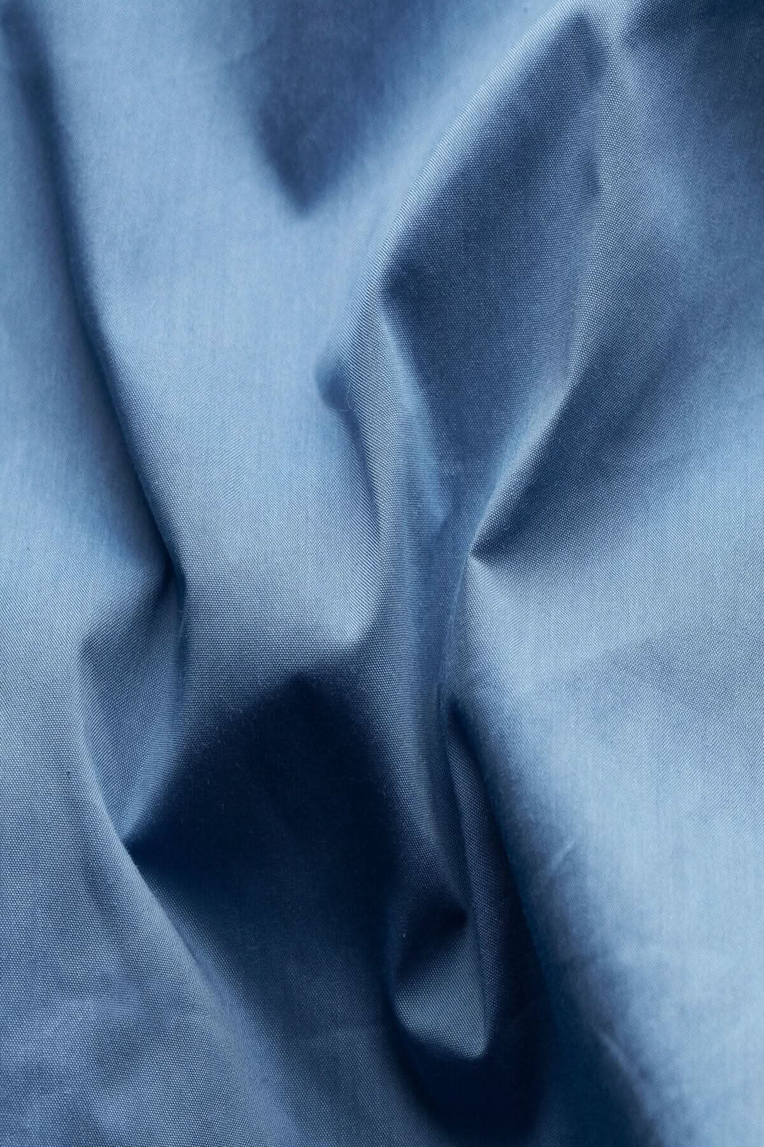 Tissu en coton bleu déperlant, présentant une texture douce et pliée, idéal pour une veste élégante.