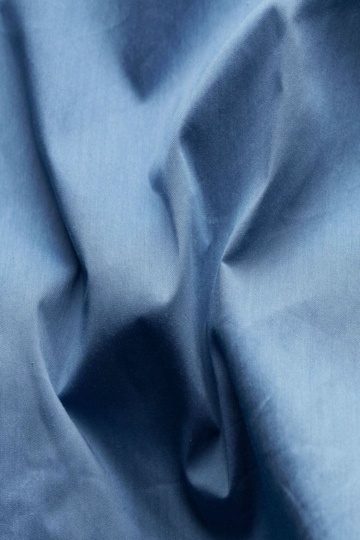 Tissu en coton bleu déperlant, présentant une texture douce et pliée, idéal pour une veste élégante.