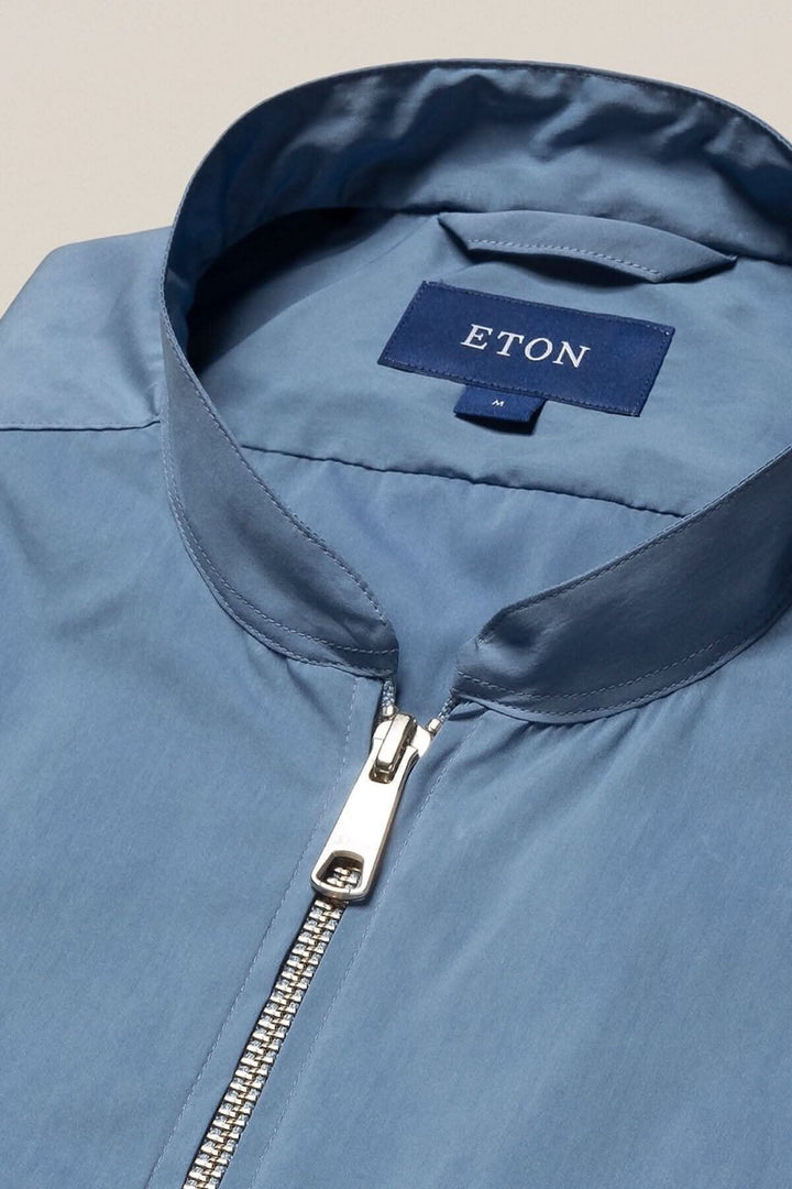 Détail d'une chemise bleue Eton avec col montant et fermeture éclair en métal.