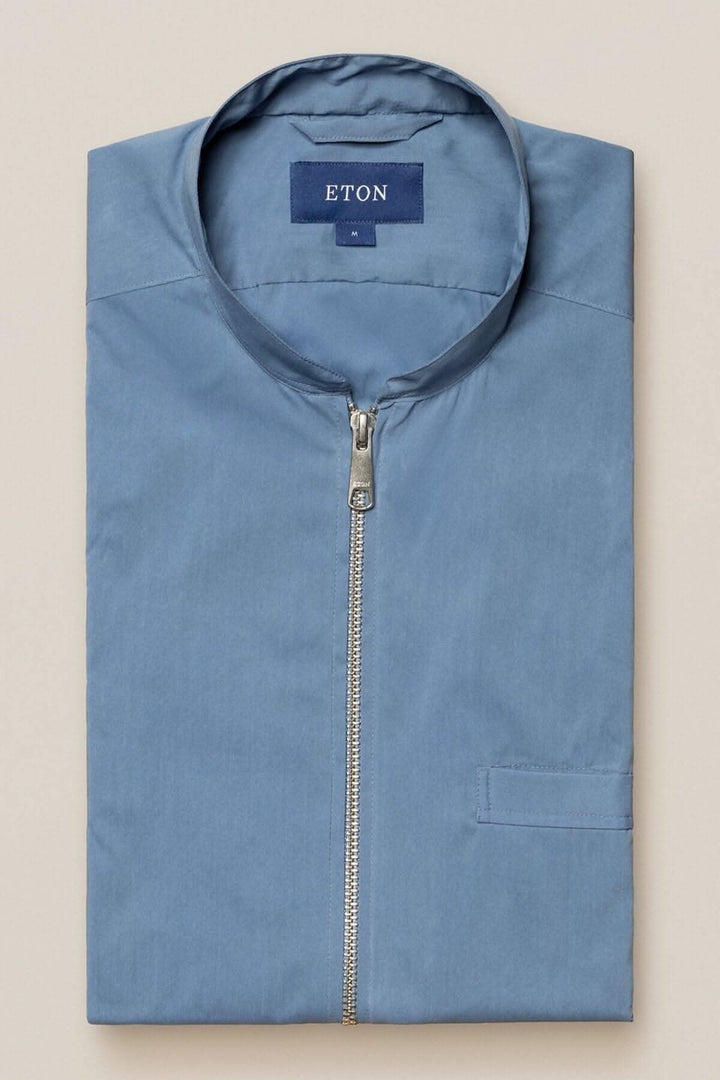 Chemise Eton bleue, élégante, avec col montant et fermeture éclair, pliée sur une surface claire.