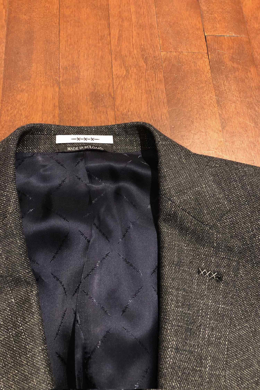 Veston gris Van Gils avec doublure soyeuse et détails raffinés sur fond en bois.